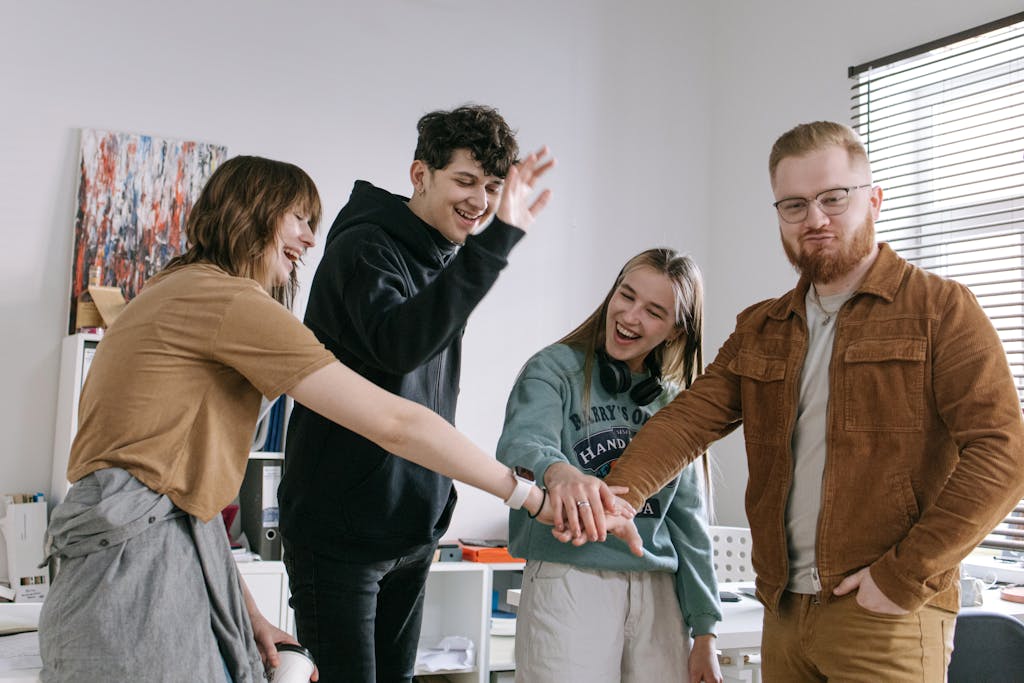 A group of cheerful young colleagues celebrating with a team hand stack indoors.