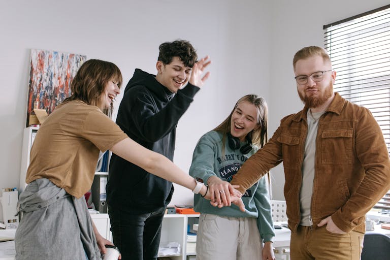 A group of cheerful young colleagues celebrating with a team hand stack indoors.