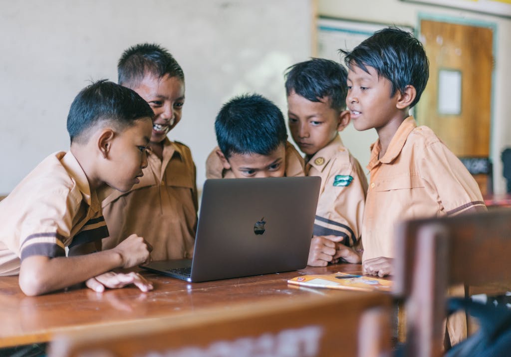 A group of young boys in school uniforms collaborating over a laptop in a classroom setting.