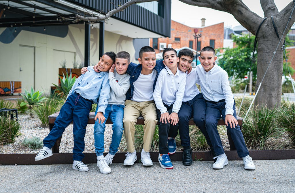 A happy group of young boys sitting together on a bench in an outdoor setting. Casual attire and friendly poses.