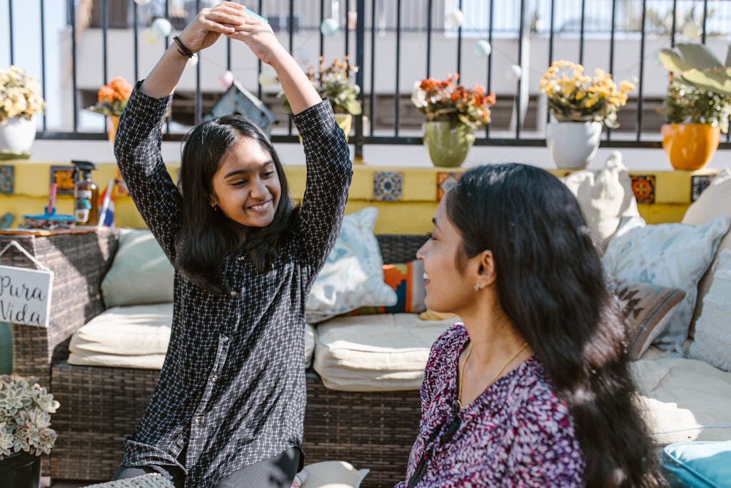 A mother and daughter share a joyful moment on a sunny day surrounded by colorful flowers.