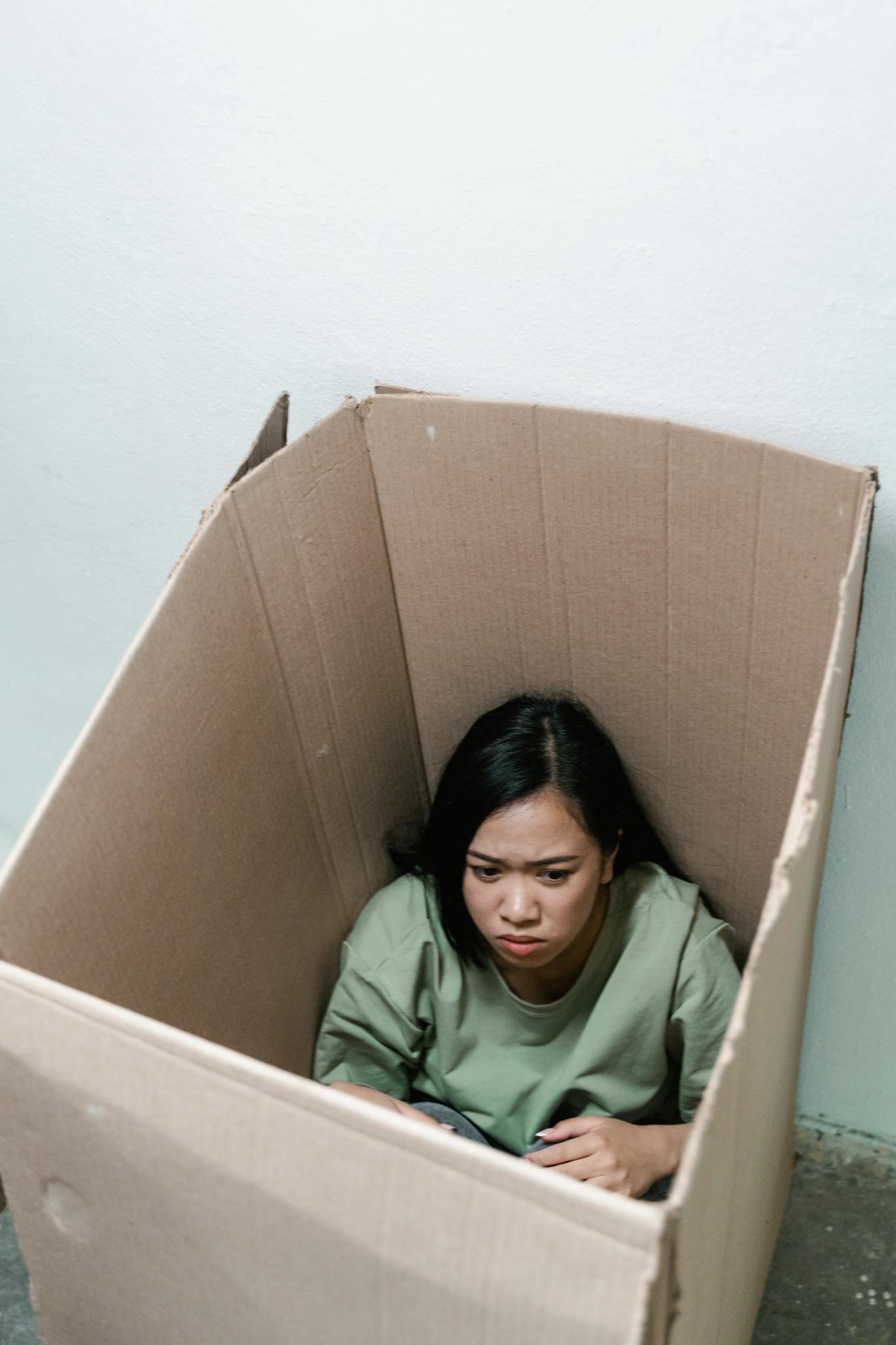 A woman sits inside a cardboard box appearing anxious, symbolizing feelings of claustrophobia.