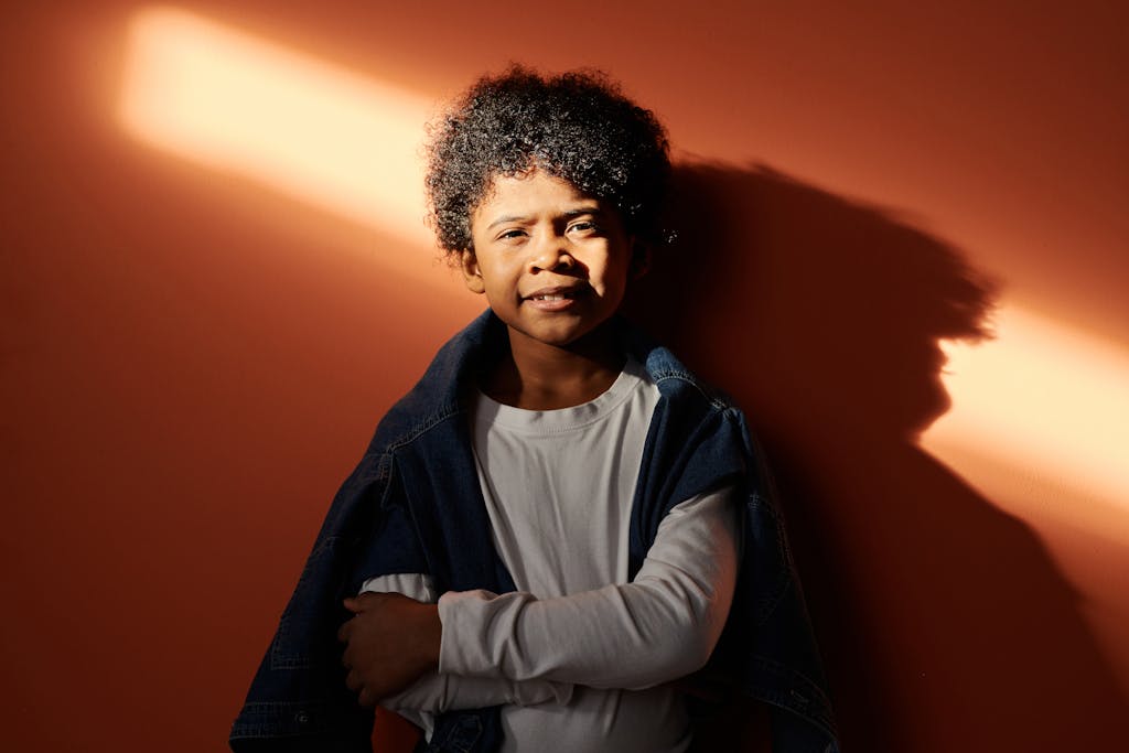 A young boy stands confidently against an orange wall, bathed in warm sunlight.