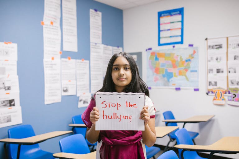 A young girl in a classroom holding a 'Stop the Bullying' sign, promoting awareness.