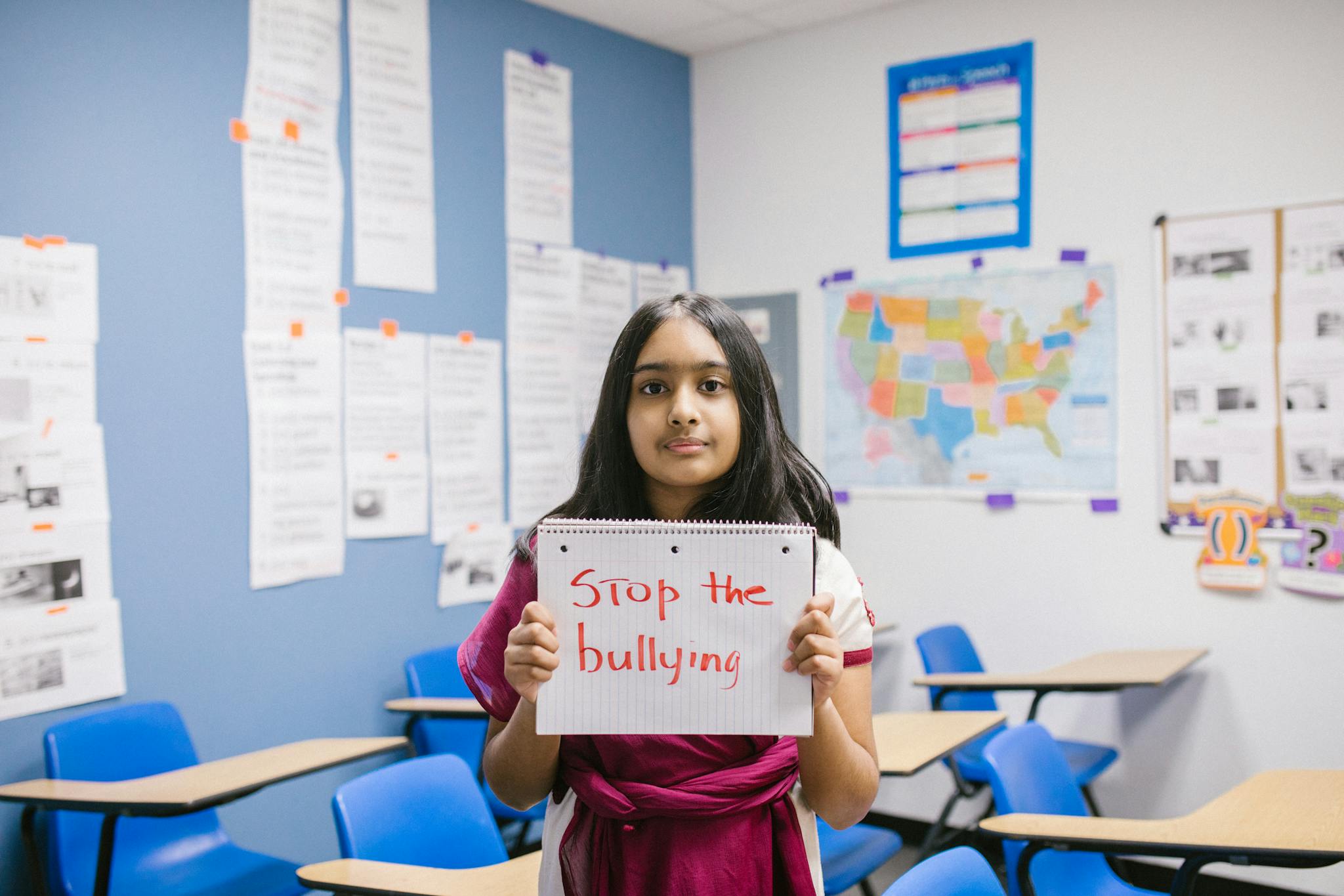A young girl in a classroom holding a 'Stop the Bullying' sign, promoting awareness.