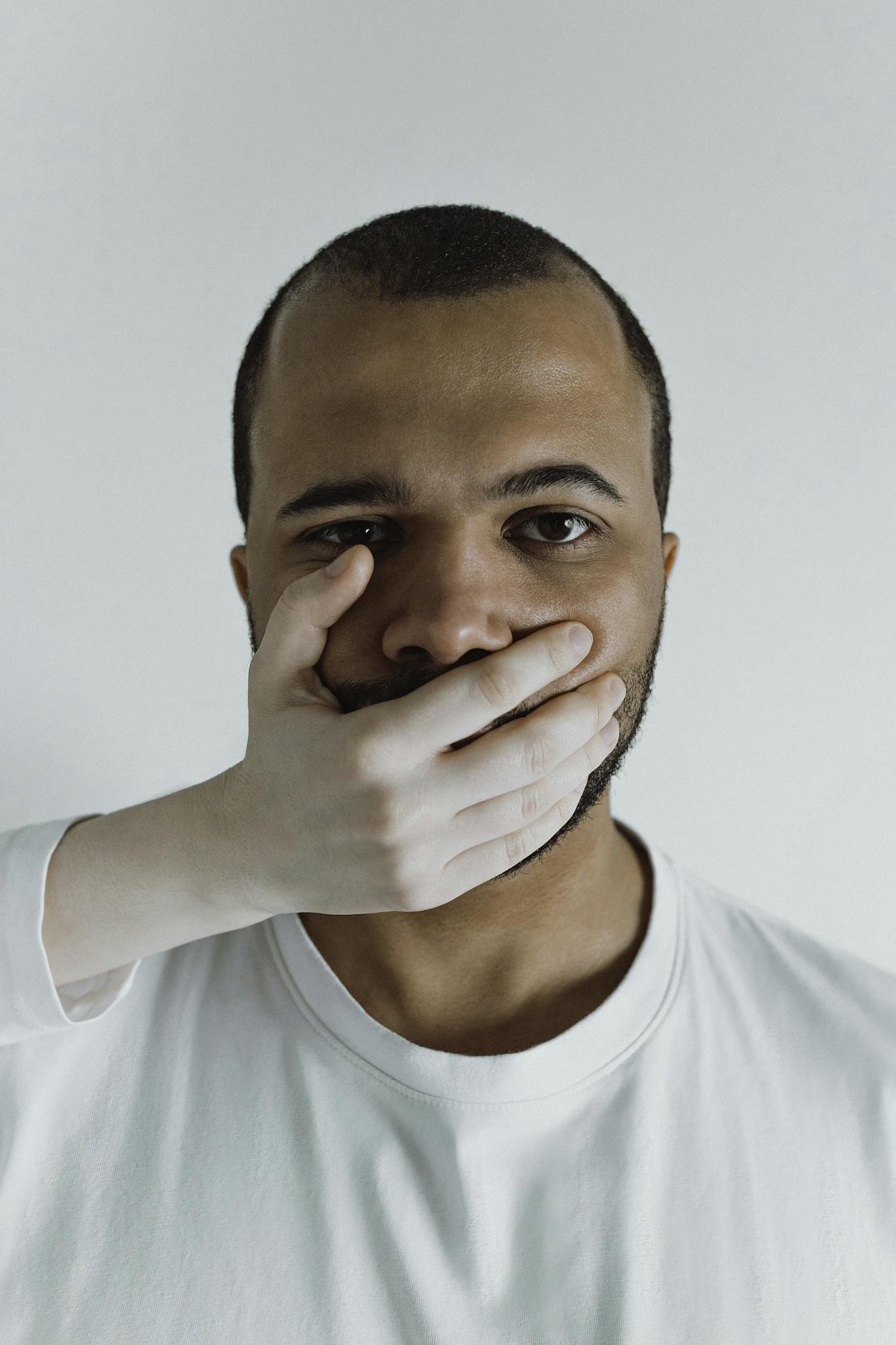 Conceptual close-up of a man with a hand covering his mouth, symbolizing silence or restraint.