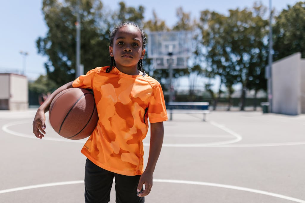 Confident child holding a basketball on an outdoor court during daytime.