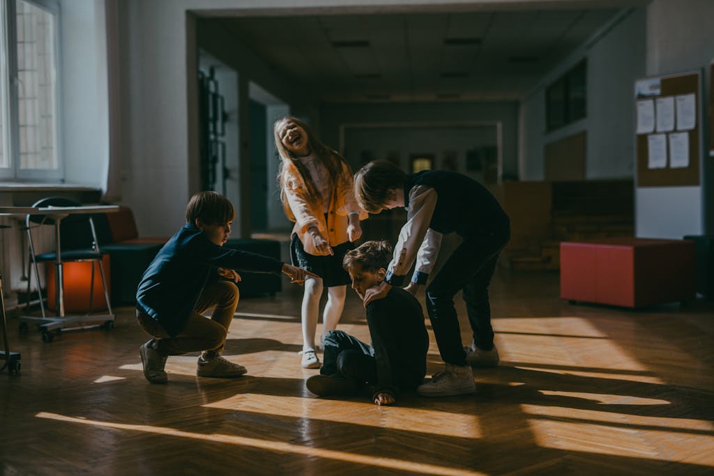 Group of children in a school setting pointing at a seated boy, highlighting school bullying dynamics.