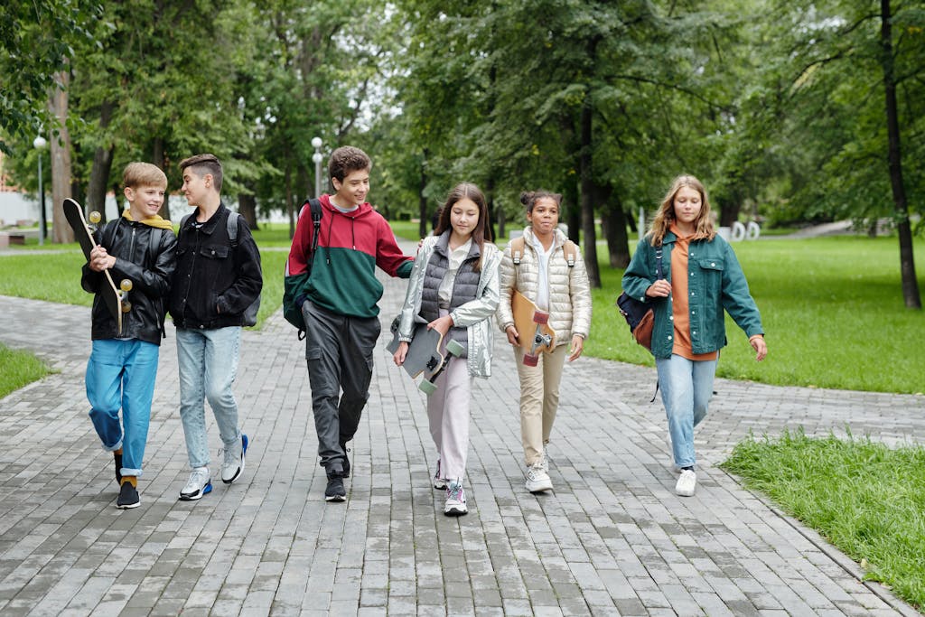 Group of teenagers walking and laughing together in a sunny park setting.