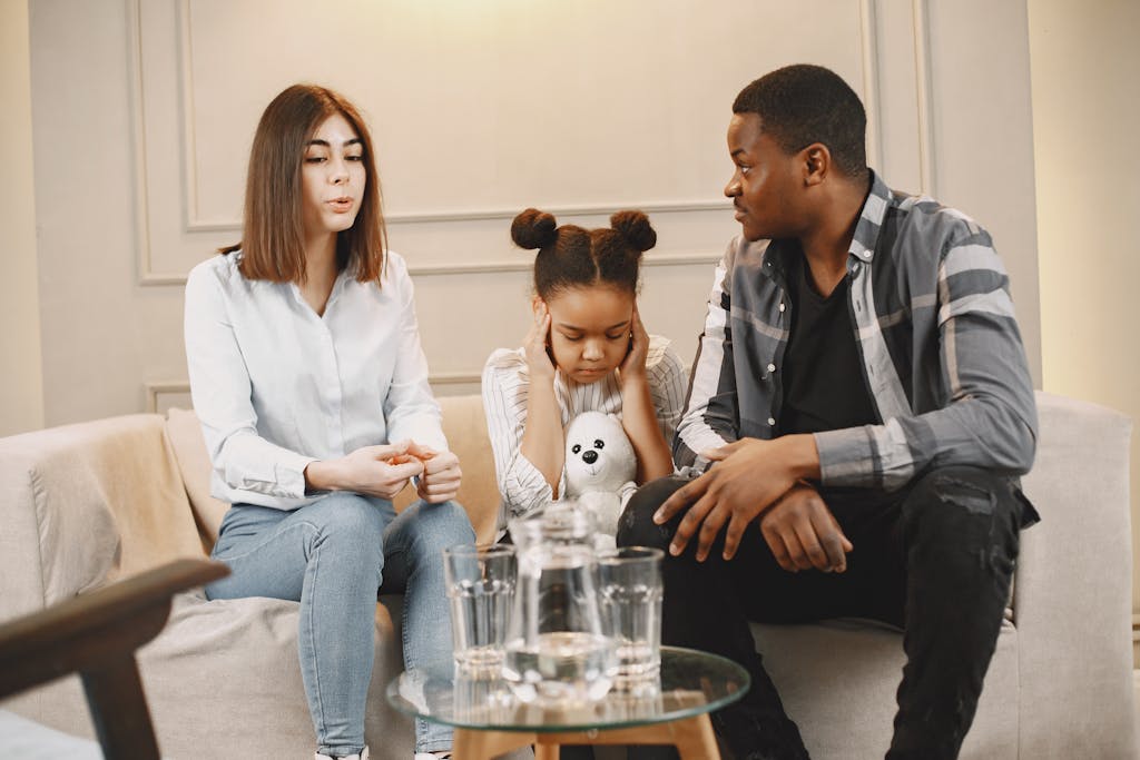 Parents talking to daughter covering ears on sofa.