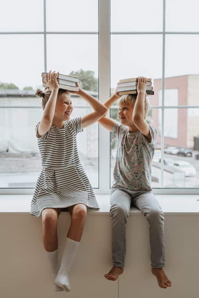Children balancing books on their heads and laughing together in class
