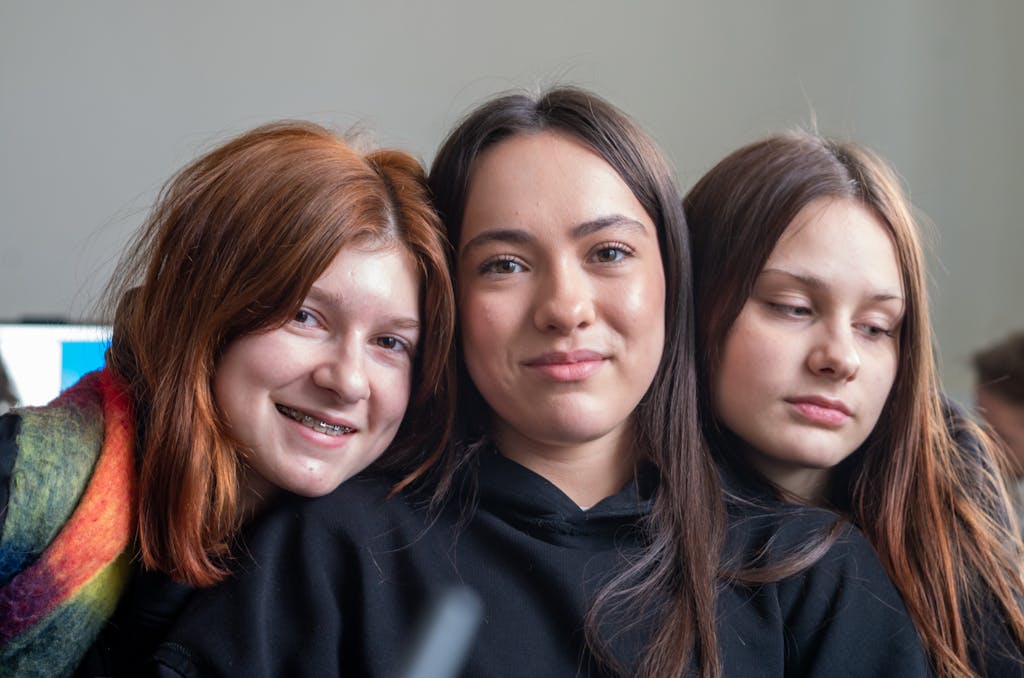 Three teenage girls smiling and posing together, showcasing friendship and youth indoors.