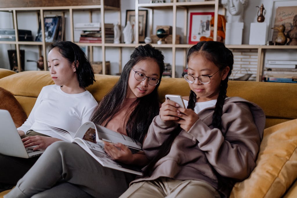 Three women enjoying leisure time on a sofa with a laptop and cellphone, creating a warm family atmosphere.