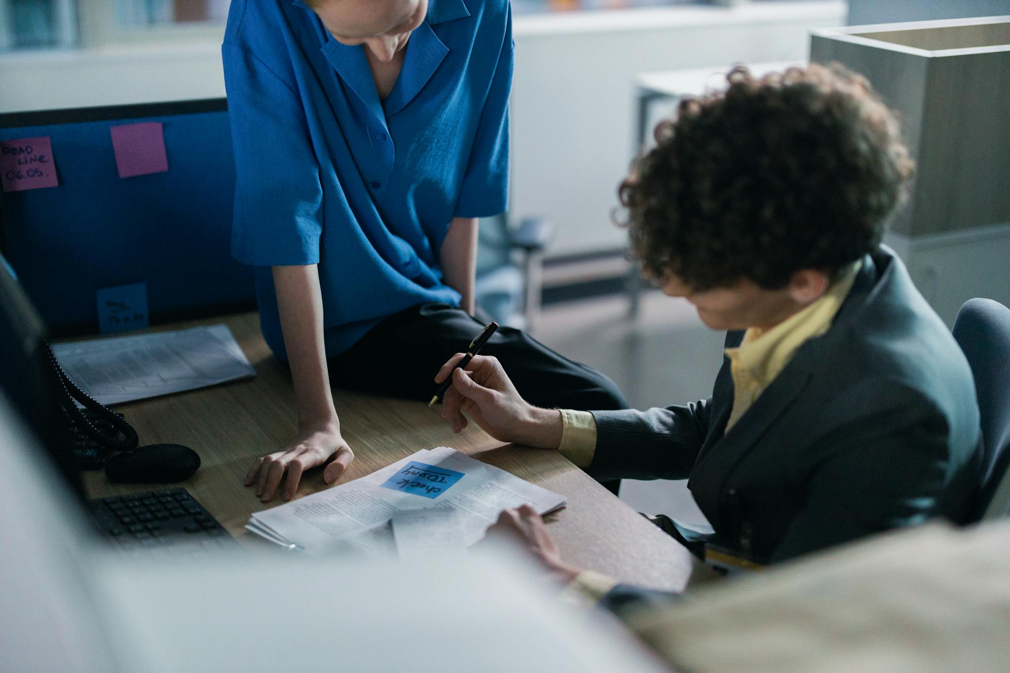 Two colleagues in a modern workspace discussing and writing notes during a meeting.