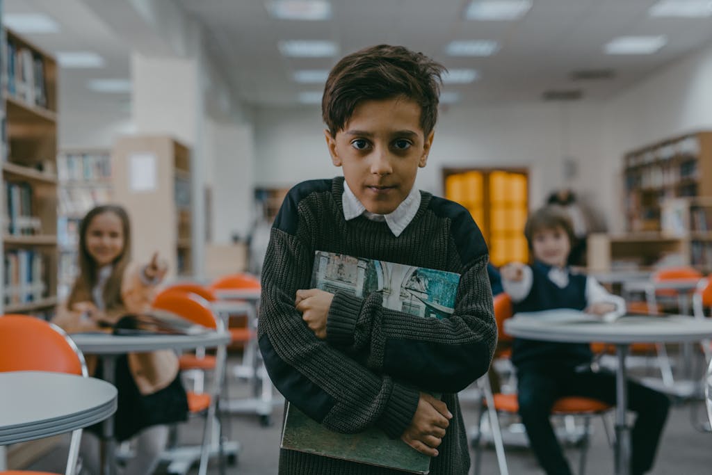 Young boy in school library looking sad while classmates point and laugh.