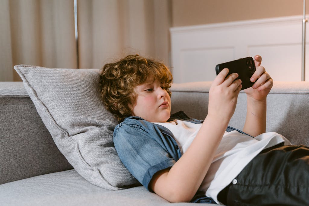 Young boy relaxing on a sofa, using a smartphone, indoors.